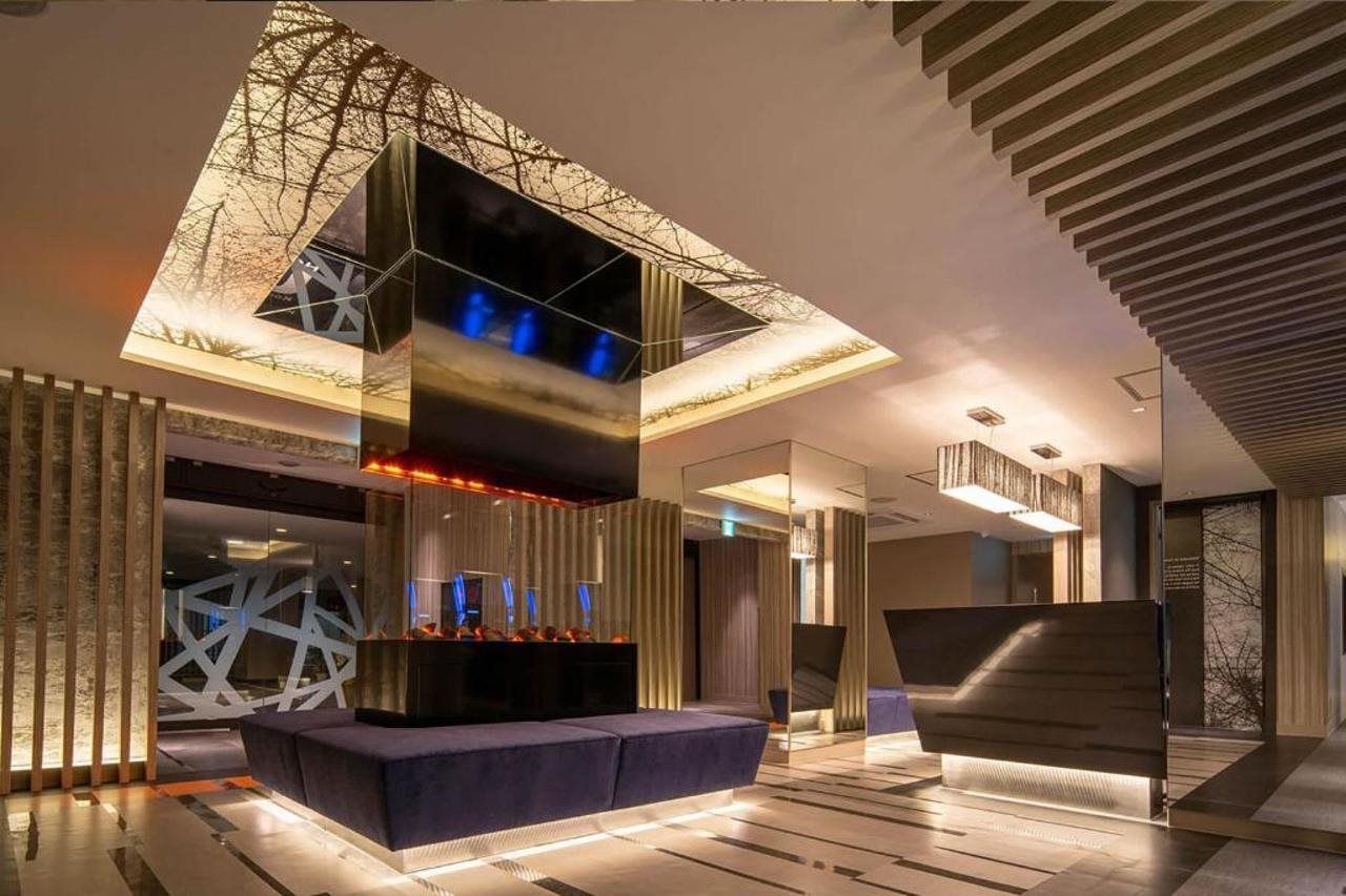 A modern interior with a central seating area, a geometric wall design, and a ceiling with a unique light fixture.