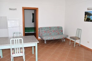 Une pièce comprenant une table à manger, des chaises, un canapé, un réfrigérateur et une porte donnant sur une autre pièce.