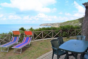 A patio with lounge chairs and a table, overlooking a coastal landscape. - San Nicola Centro Turistico (Peschici)