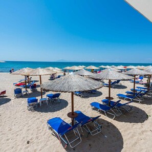Una playa con filas de sillas azules y sombrillas de paja bajo un cielo despejado.