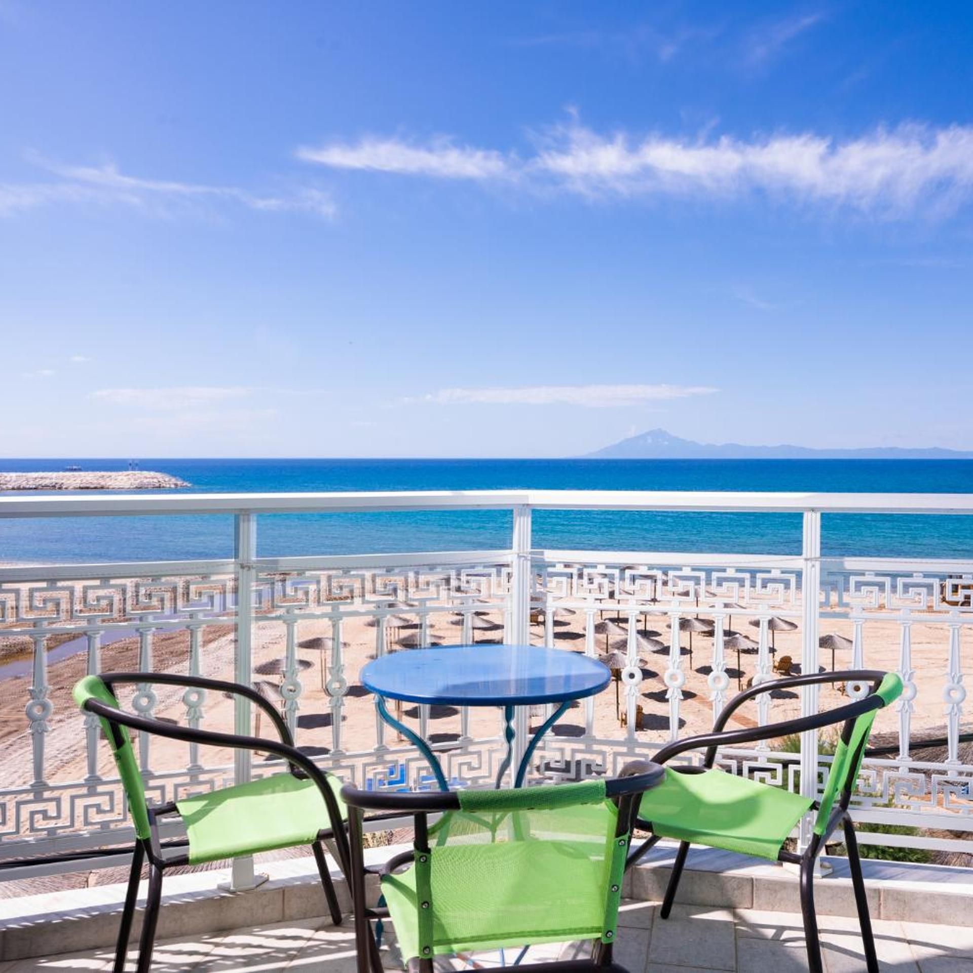 A terrace with a table and chairs overlooking a beach and the sea.