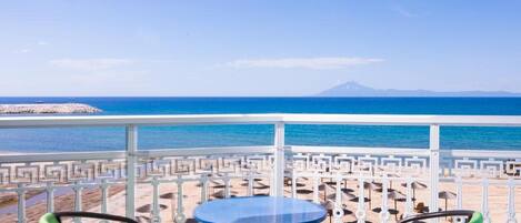 A terrace with a table and chairs overlooking a beach and the sea.