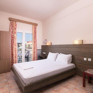 Habitación de hotel con cama, cabecero de madera, cortinas, una mesita y una silla.