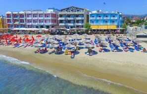 A beach with rows of sun loungers and umbrellas, a building with balconies, and a clear view of the sea. - Ralitsa Hotel (Thasos)