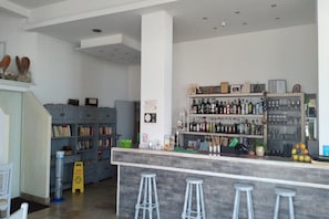 Una zona de bar con mostrador, taburetes, estantes con botellas y una estantería.