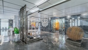 Un vestíbulo moderno con piso de mármol, un mostrador de recepción y una gran esfera decorativa.