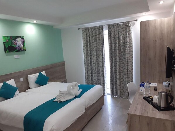 A hotel room with a bed, a desk, a chair, a television, and a window with curtains. - TJ Boutique (Marsaskala)