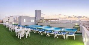 A rooftop pool area with lounge chairs and tables, surrounded by buildings. - TJ Boutique (Marsaskala)