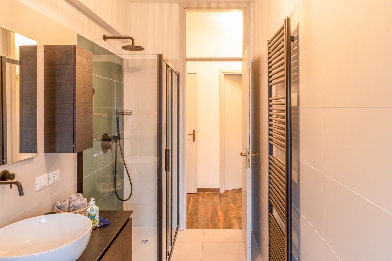 Un bagno moderno con cabina doccia in vetro, un mobile bagno in legno e uno specchio grande.