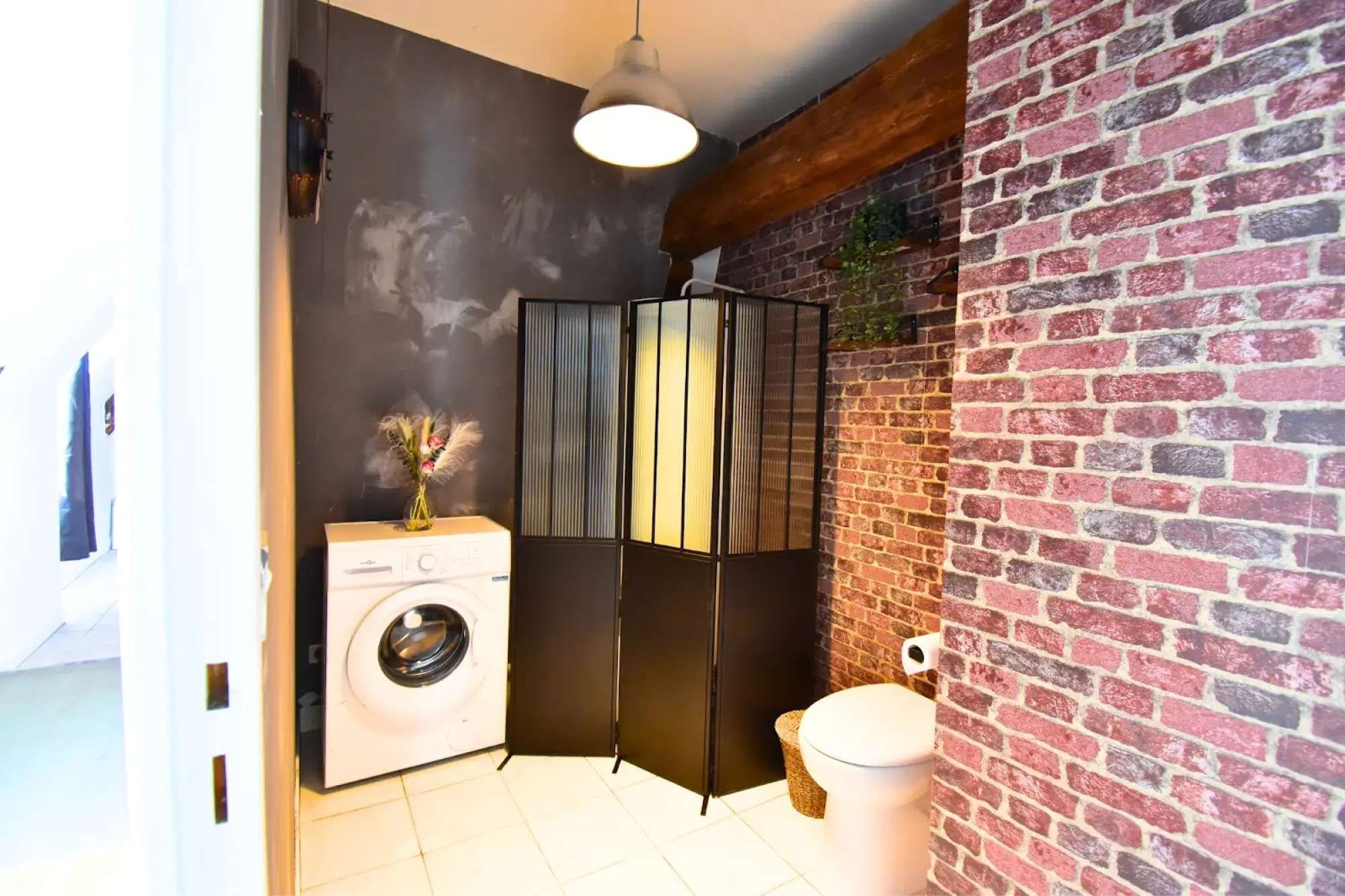 Een kleine badkamer met een wasmachine, toilet en grote spiegel.