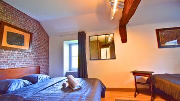 Une chambre avec un mur en briques, un lit avec une serviette enroulée, une fenêtre avec des rideaux, un miroir et une petite table.