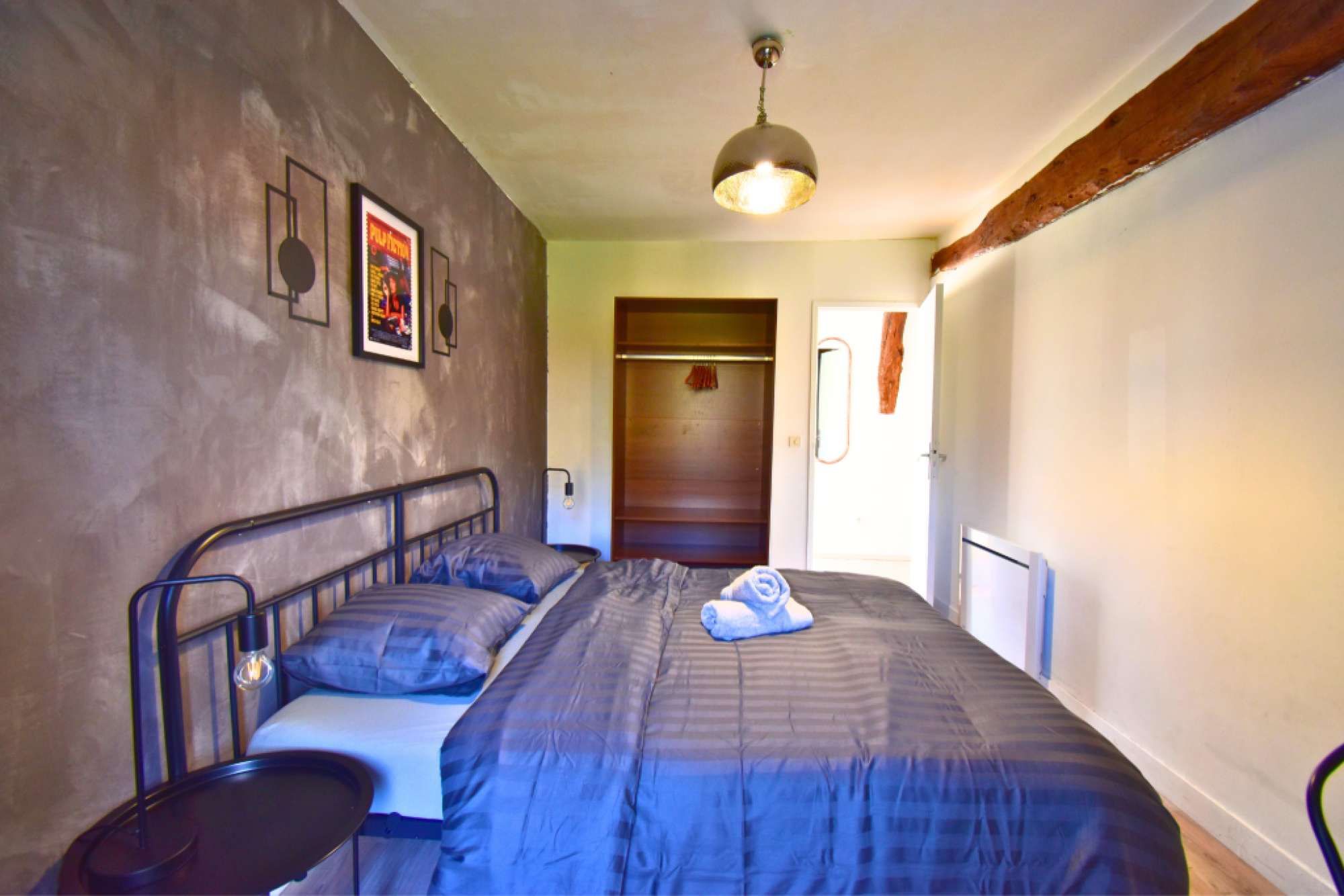 Een slaapkamer met een bed, nachtkastje, kledingkast en hanglamp.