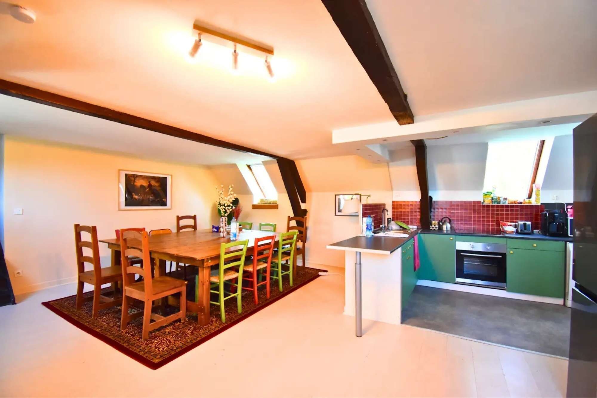 A dining area with a wooden table and chairs, a kitchen with green cabinets and a built-in oven, and a window providing natural light.
