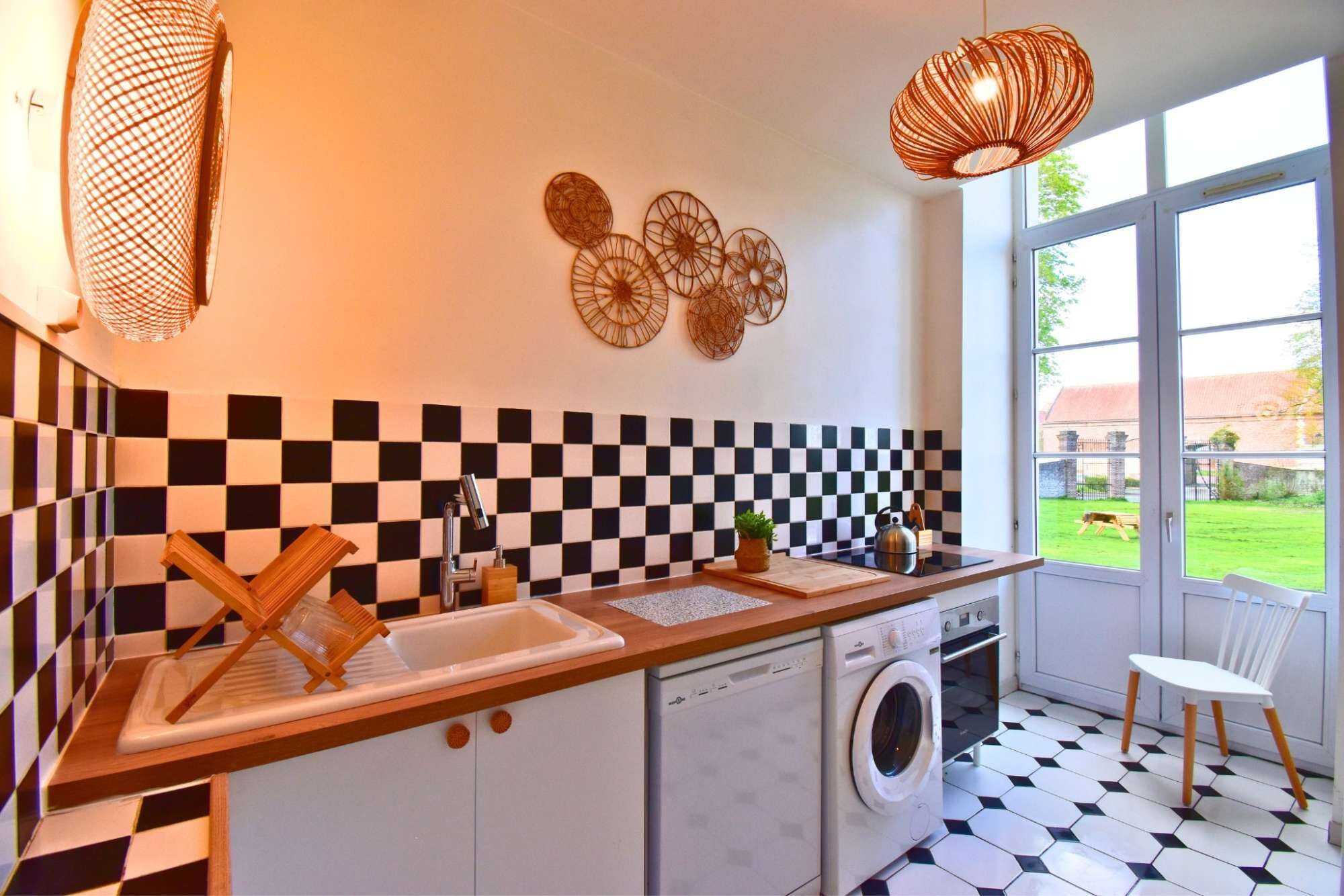 Een keuken met een zwart-wit betegelde achterwand, een wasmachine en een raam met uitzicht op een groen gazon.