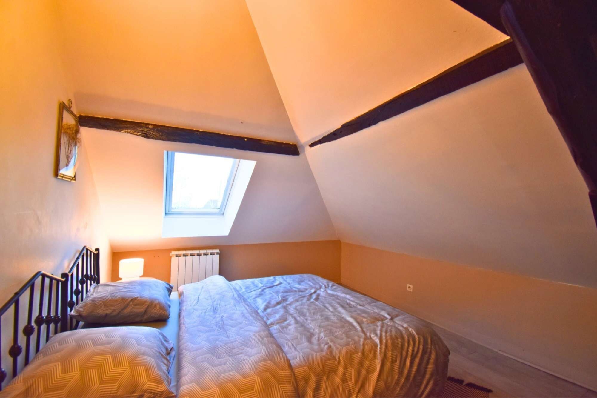 Een slaapkamer met een schuine kap, dakraam, een bed met beddengoed met een patroon en een radiator.