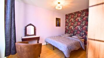 Une chambre à coucher comprenant un lit, une chaise, une commode, un miroir et un papier peint à motifs floraux.