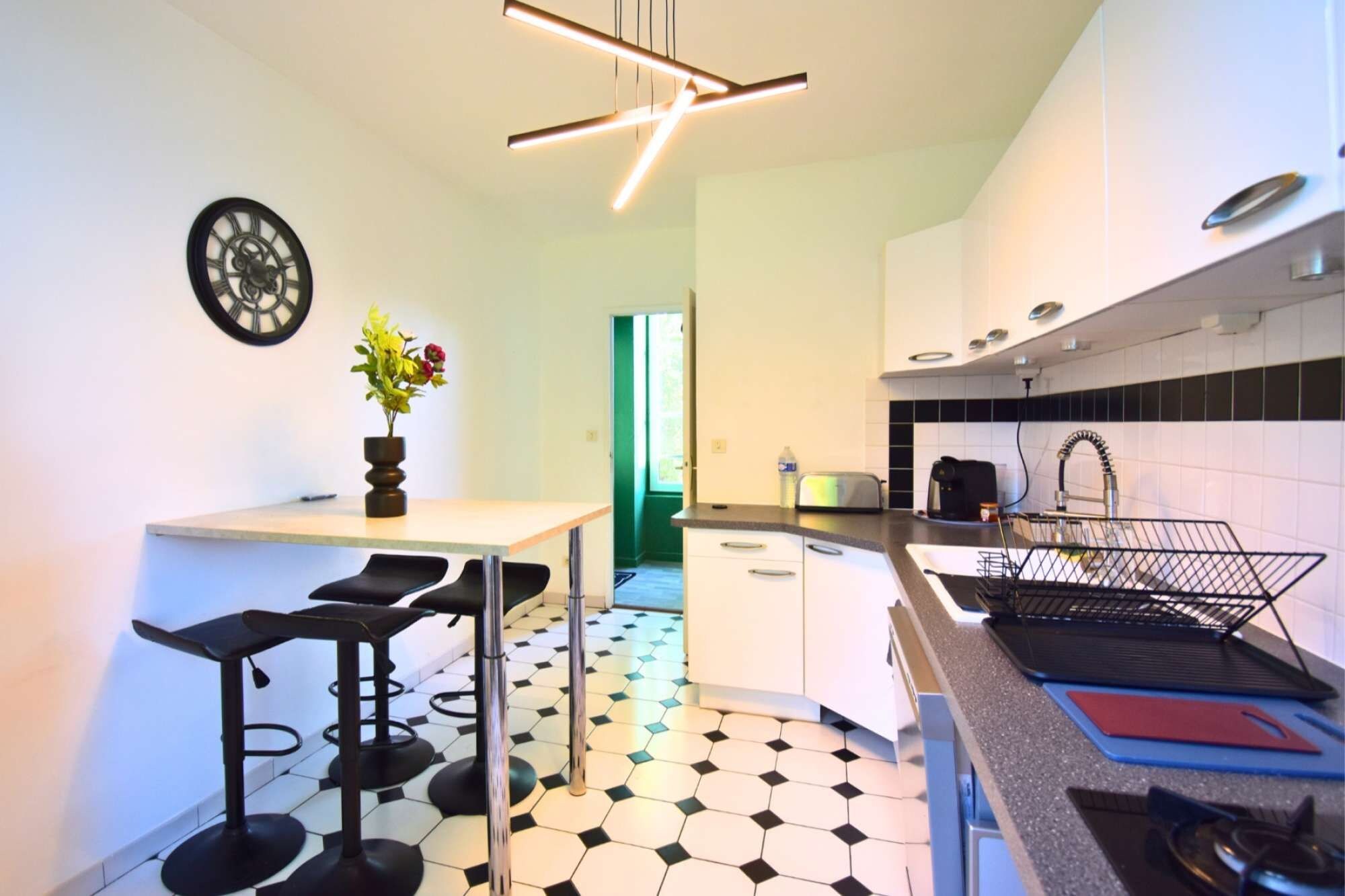 Une cuisine moderne avec un sol carrelé en noir et blanc, un coin repas avec des tabourets de bar et une horloge murale.