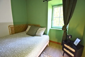 A room with a bed, a window with curtains, and a bedside table with a lamp.