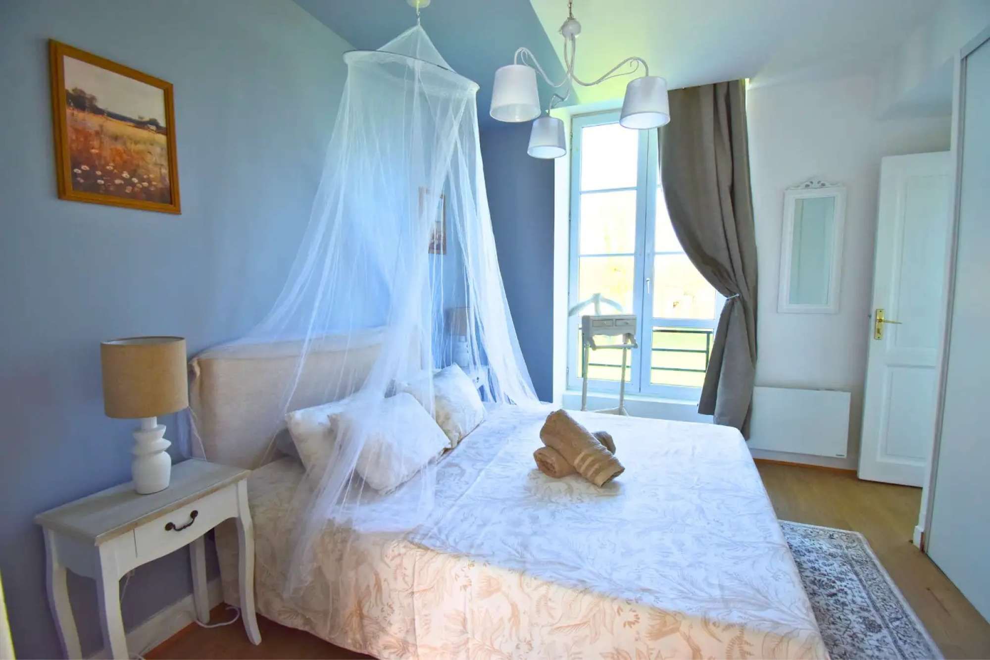 Een slaapkamer met een bed, nachtkastje, lamp en een raam met gordijnen.