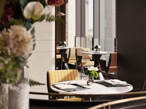A restaurant with round tables, wicker chairs, and a vase with flowers. - Novotel Zibo New Hongcheng (Zibo)