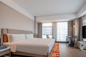 Una habitació d'hotel amb un llit, una taula de nit, una cadira, un televisor i una finestra amb cortines.