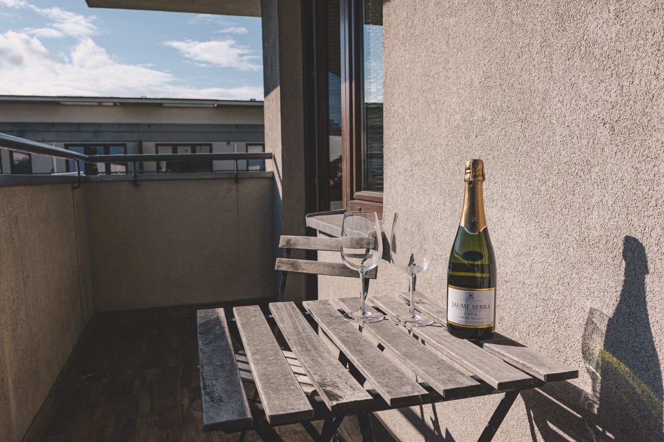 Een balkon met een houten tafel, een fles wijn en twee glaasjes.