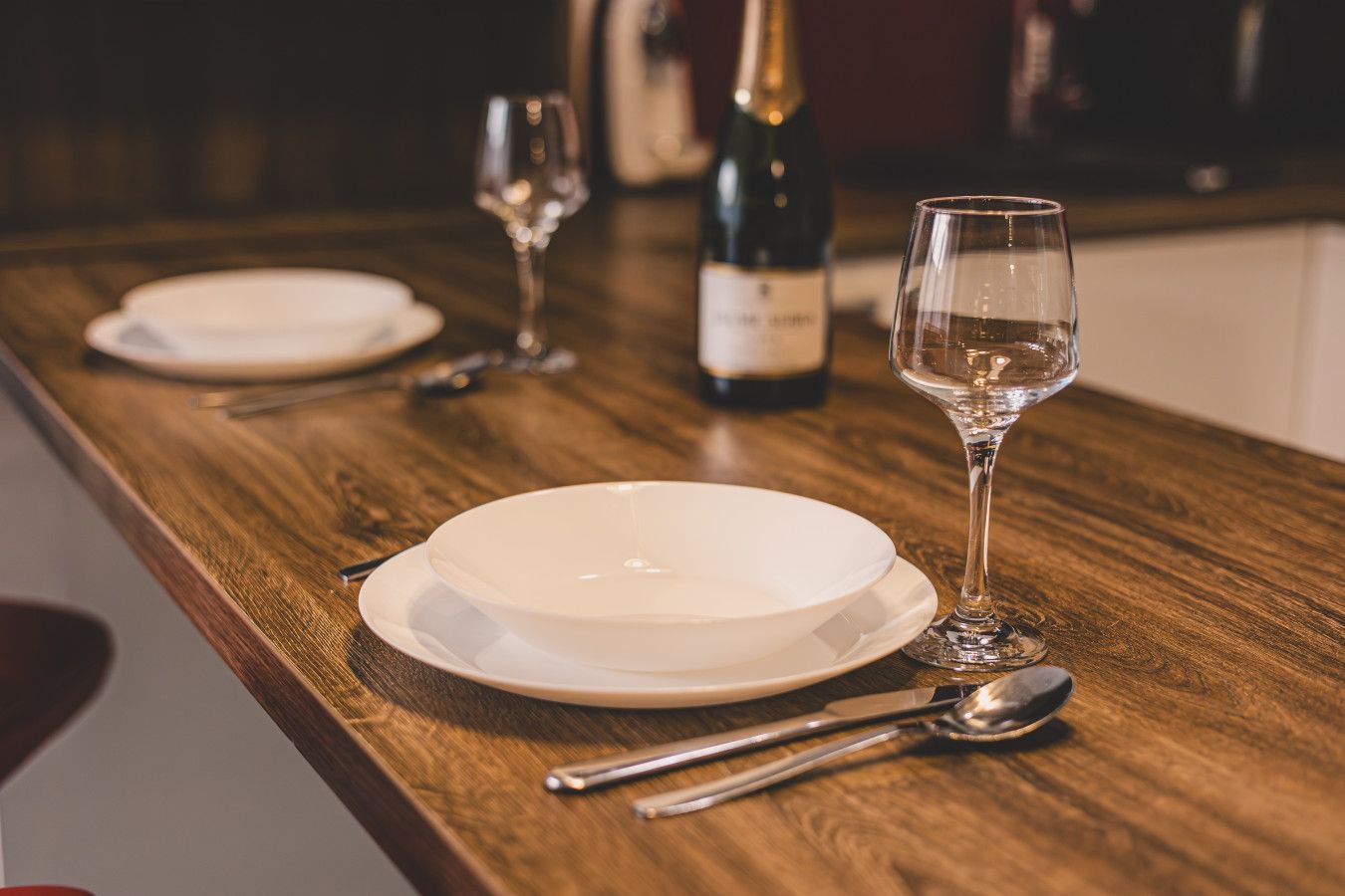 Une table en bois, avec une assiette blanche, un verre à vin et une bouteille de vin.
