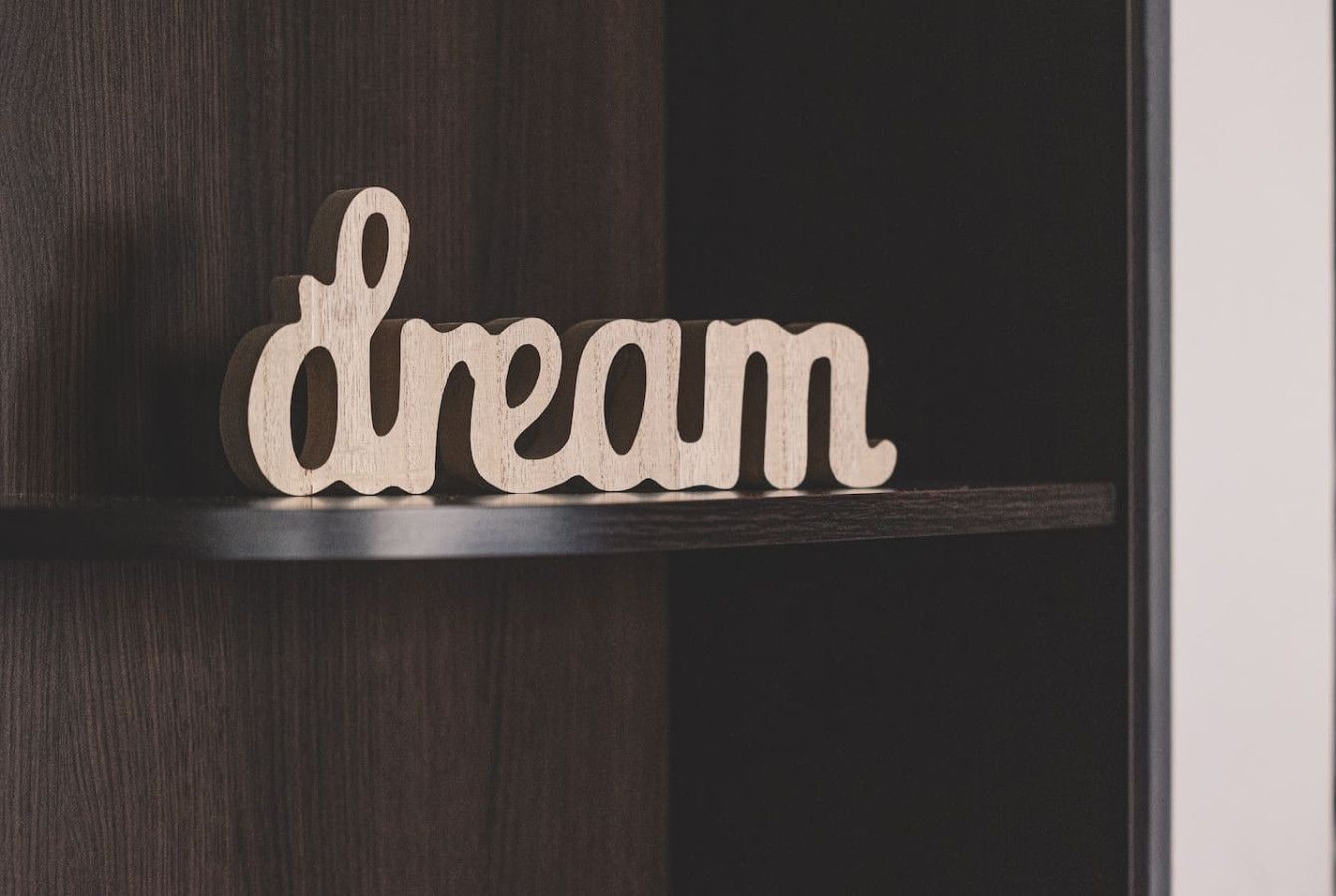 A wooden sign with the word 'dream' on a dark wooden shelf.