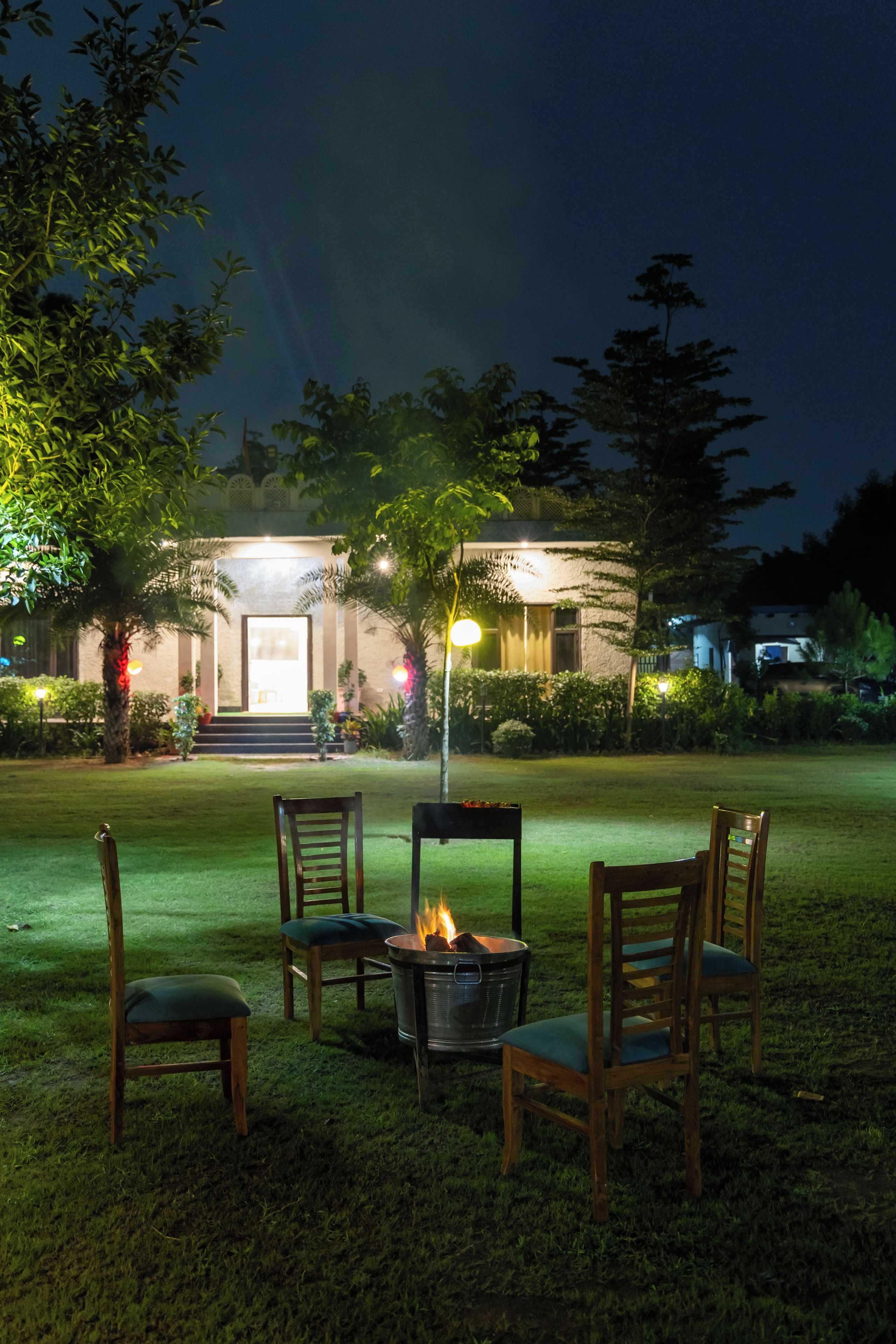 An outdoor seating area with chairs and a fire pit, surrounded by a well-maintained lawn and trees, under a night sky.