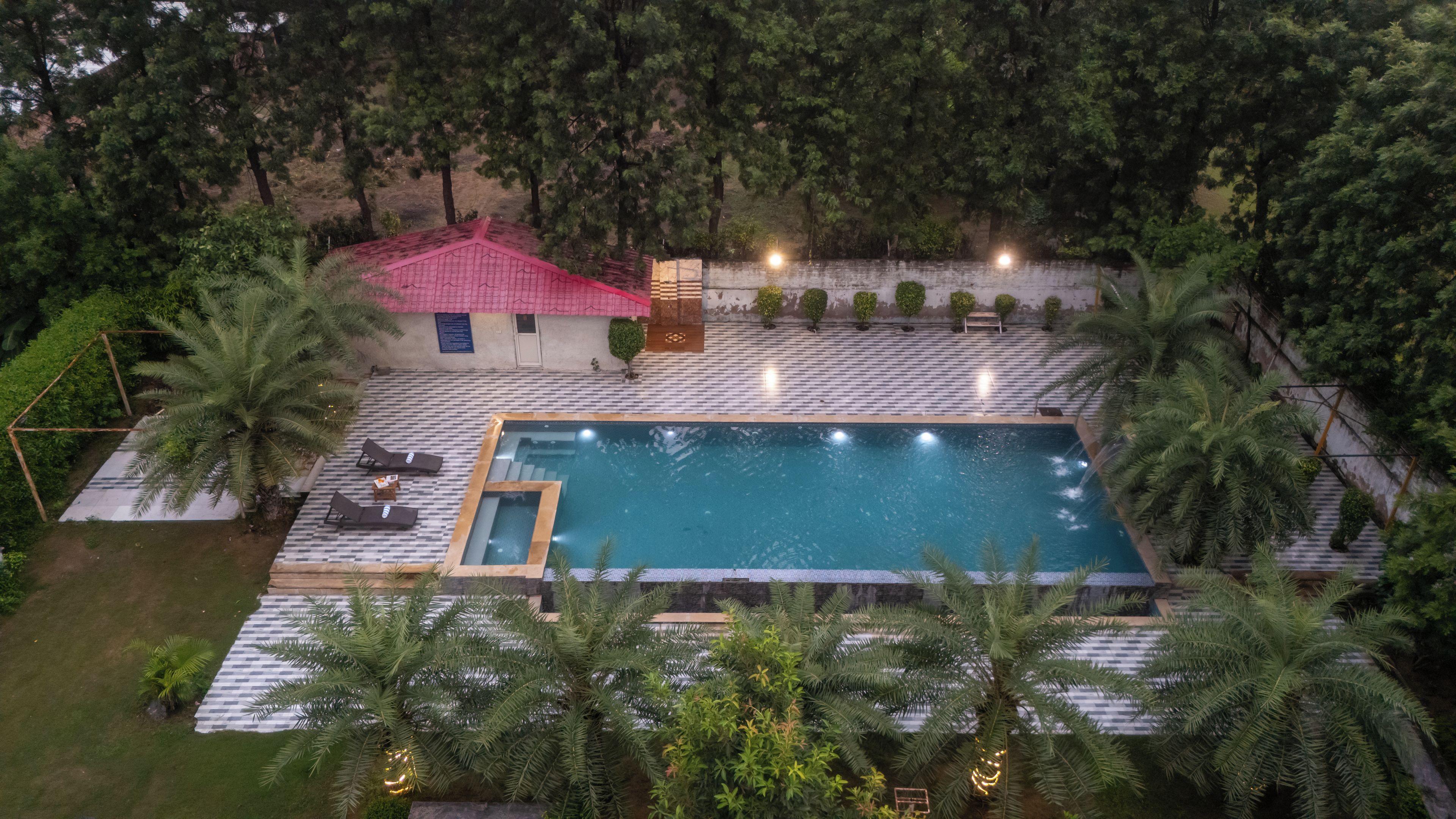 Una piscina con borde de baldosas, rodeada de palmeras y un edificio de techo rojo.