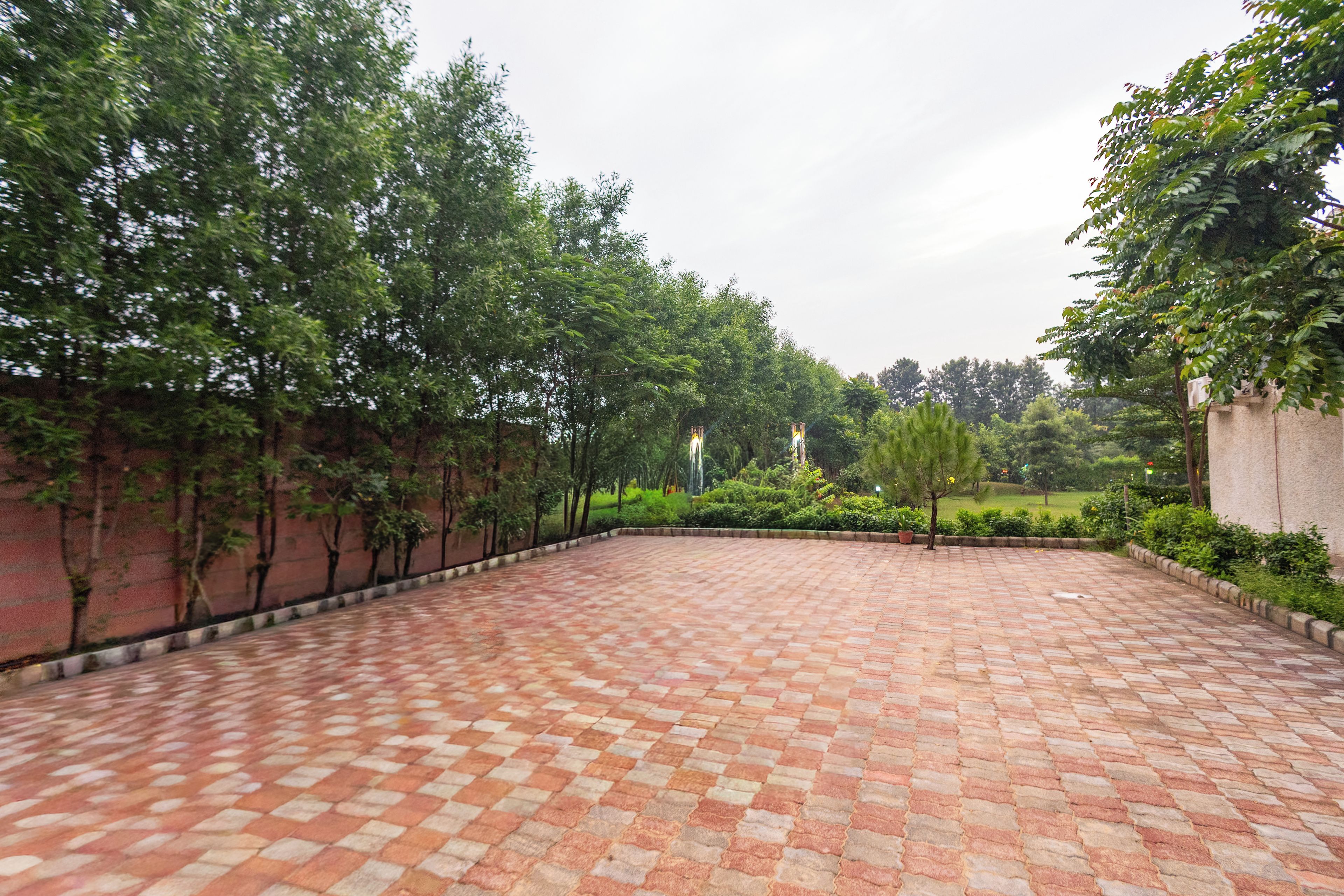 A paved courtyard with a brick pattern, surrounded by trees and a low wall.