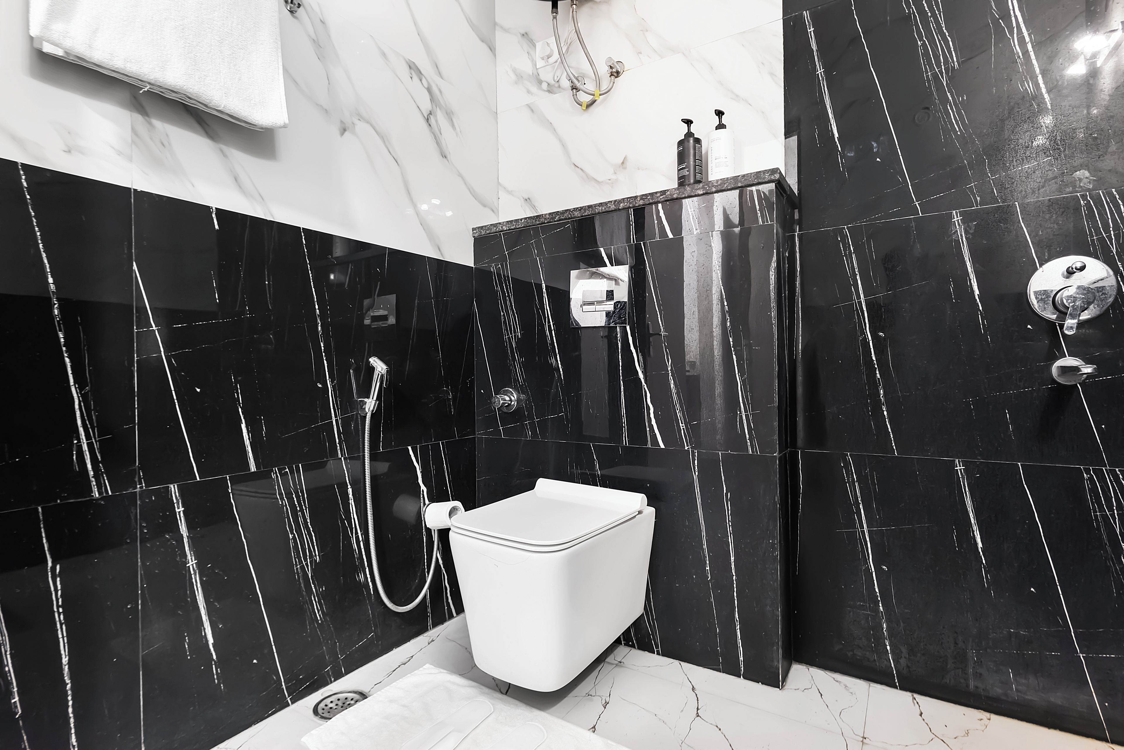 A bathroom with a white toilet, black marble walls, and a shower area.