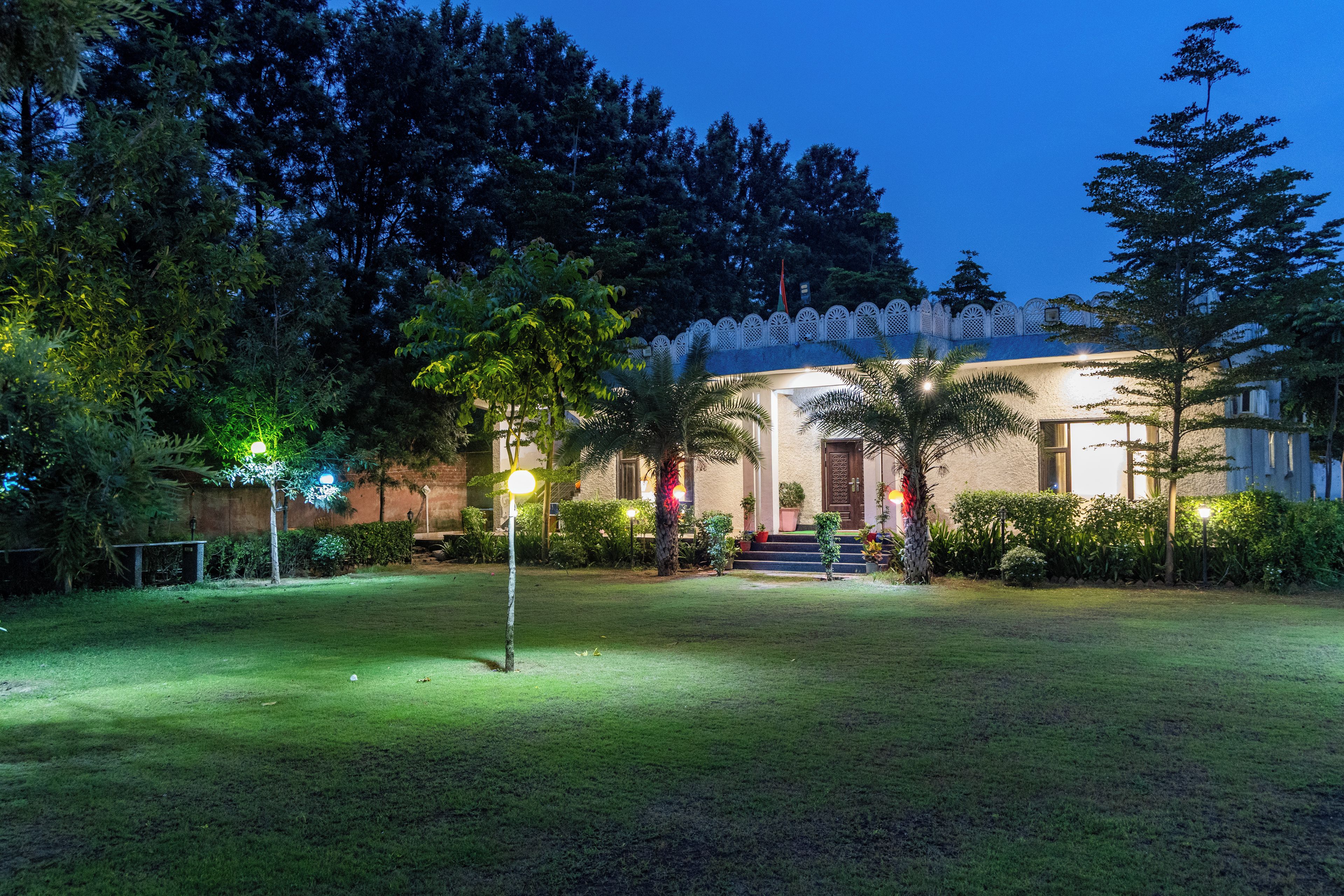 A well-lit building with a porch, surrounded by trees and a grassy lawn.
