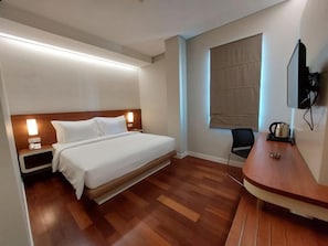 A hotel room with a bed, bedside tables, a desk, a chair, and a television. - The Point Hotel Balikpapan (Balikpapan)