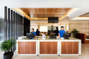 A reception desk with a modern design, a flat-screen TV mounted on the wall, and a potted plant on the left. - The Point Hotel Balikpapan (Balikpapan)
