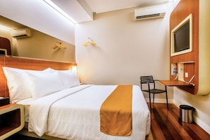 A hotel room with a bed, bedside table, chair, TV, and a small desk. - The Point Hotel Balikpapan (Balikpapan)