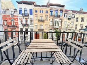 A balcony with wooden benches and a metal railing overlooking a row of multi-story buildings with various architectural styles. - Modern in the Heart of Brussels (Bruxelles)