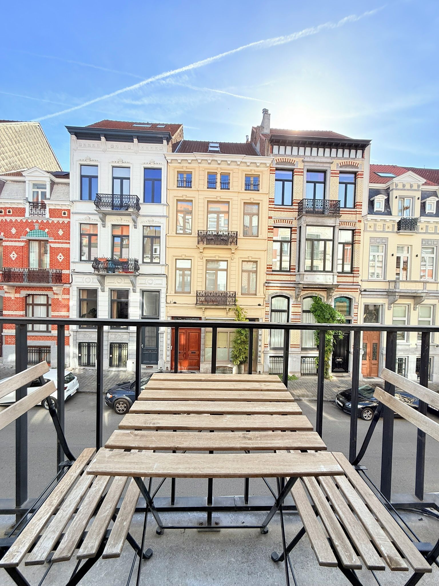 A balcony with wooden benches, overlooking a row of multi-story buildings with various architectural styles.