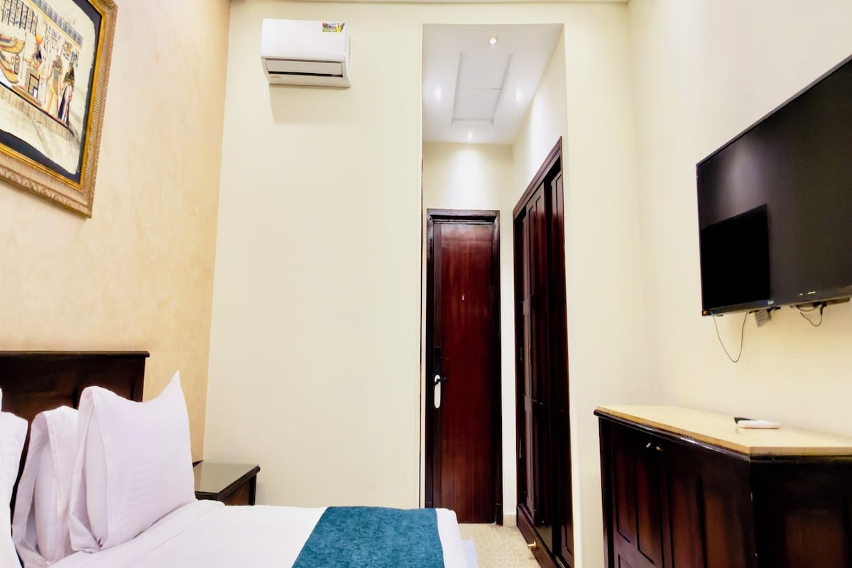 A hotel room with a bed, a television, an air conditioning unit, and a door leading to another room.