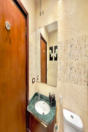 A bathroom with a wooden door, a sink with a marble countertop, a mirror, and a toilet. - Bafana Pyramids Hotel & Spa (Giza)