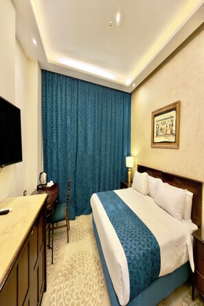 A hotel room with a bed, a desk, a chair, a television, and a painting on the wall. - Bafana Pyramids Hotel & Spa (Giza)