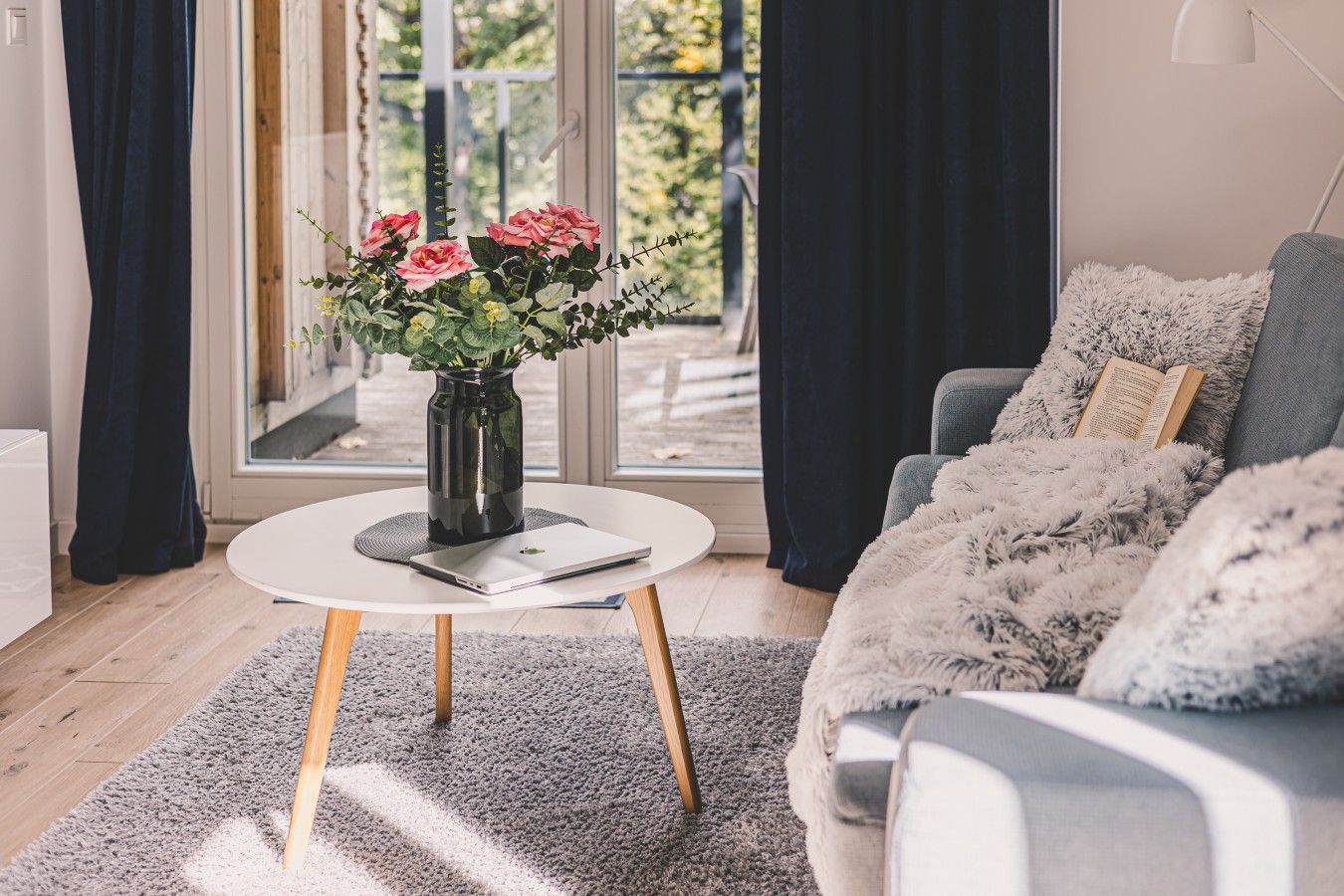 Een moderne woonkamer met een ronde salontafel, een laptop, een vaas met bloemen en een bank met een zachte plaid.