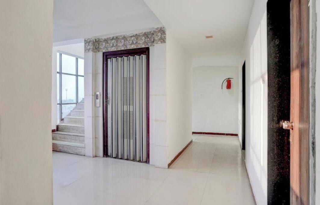Un pasillo con una escalera que conduce a una plataforma, una puerta con pomo vertical y un extintor de incendios fijado en la pared.