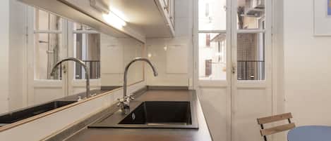 A kitchen with a double sink, a mirror, and a view of the outside.