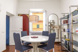 A dining area with a round table, four chairs, a hanging lamp, and a view of a building through a window. - Bernini in Cavour - Monti District (Rome)