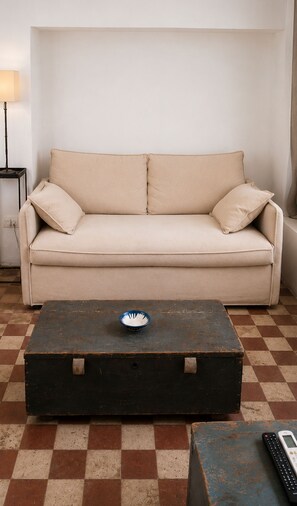 A beige sofa with two pillows, a dark wooden coffee table with a blue bowl, and a remote control on a checkered floor. - An authentic Salento home with a private courtyard, in the heart of Salento (Giuliano Di Lecce)