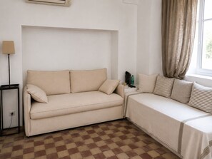 A room with a beige sofa, a small side table, a lamp, and a window with curtains. - An authentic Salento home with a private courtyard, in the heart of Salento (Giuliano Di Lecce)