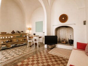 A living room with a fireplace, a television, and a bookshelf with various items. - An authentic Salento home with a private courtyard, in the heart of Salento (Giuliano Di Lecce)