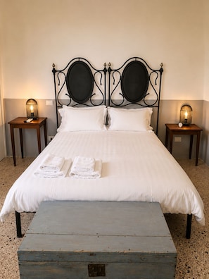 A bed with white linens, two bedside tables with lamps, and a wooden bench in front. - An authentic Salento home with a private courtyard, in the heart of Salento (Giuliano Di Lecce)