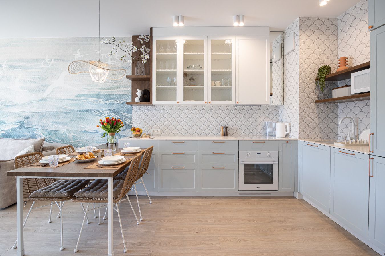 A modern kitchen with white cabinetry, a built-in oven, and a dining area with a table set for two.